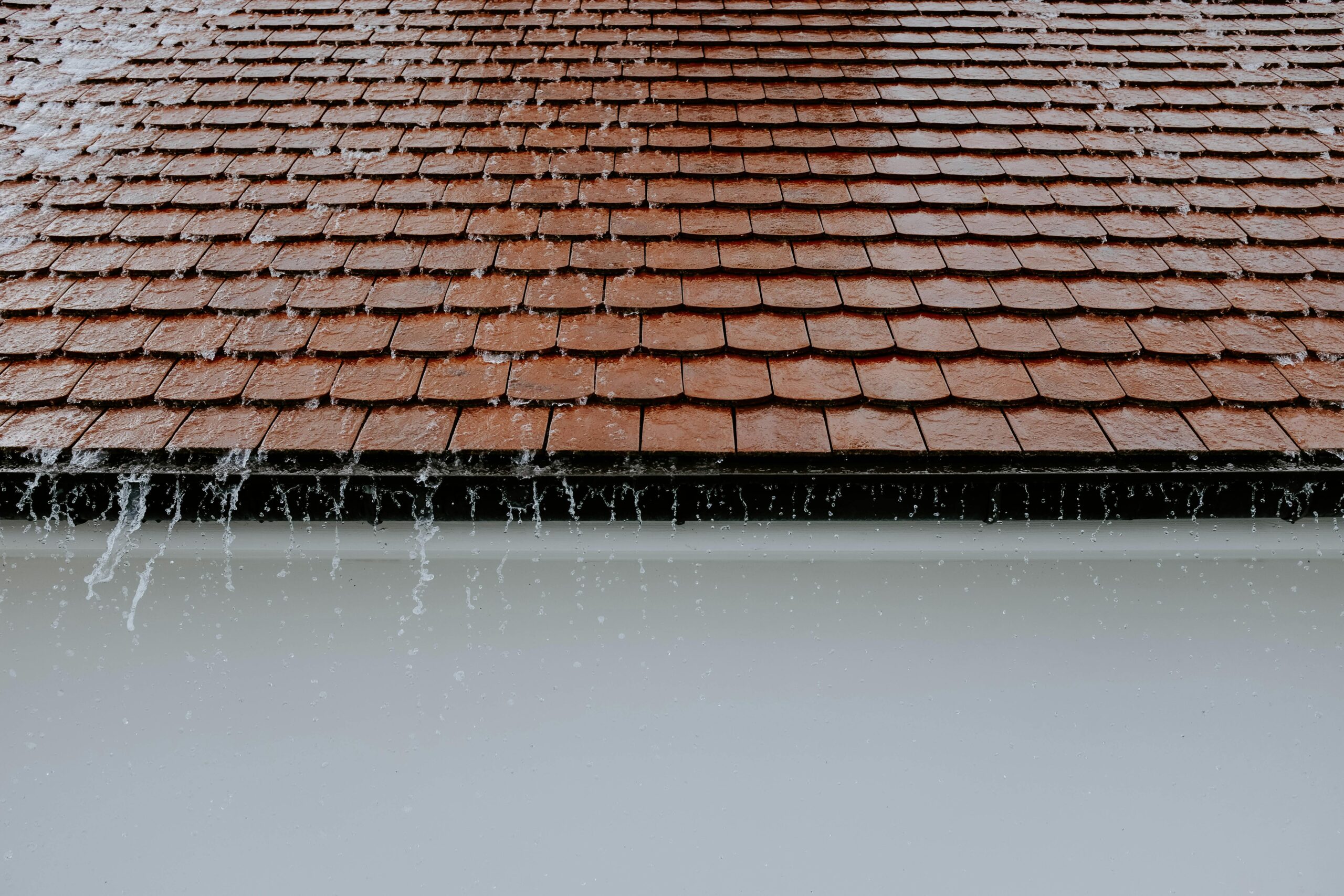 Roofing advice for homes in austin texas. Water leaking down roof top of home made of red rof and white walls.